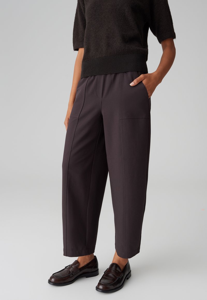 Pantaloni alti grigio scuro con tasche anteriori e dettagli di cuciture verticali. Il tessuto ha una texture liscia, una vestibilità aderente e una lunghezza cropped.