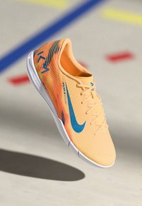 Nike Sportschuh in leuchtendem Orange mit blauen Akzenten. Verfügt über ein strukturiertes Obermaterial, eine verlängerte Form und eine leichte Sohle mit einem markanten Muster.