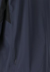 Marinblå vattentät jacka med en slät textur, svarta accenter, en minimalistisk design och "ENDURANCE"-logotyp nära fållen.