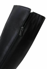 Botte noire en cuir montante avec une texture lisse et un détail de fermeture éclair sur le côté. Présente un bout arrondi et des accents cousus le long du bord.