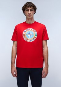 Rød bomulds t-shirt med et cirkulært grafisk motiv, der har en blå stjerne og flere nationale flag. Kortærmet og med rund hals.