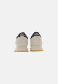 Sneakers featuring a beige suede upper, black leather heel with white text "SINCE 1890," and a cream rubber sole with textured detailing.