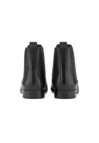 Botines de cuero negro con un acabado liso, paneles laterales elásticos y un tirador en la parte posterior. Tacón bajo apilado y silueta elegante.