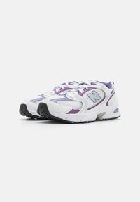 Białe i fioletowe buty sportowe New Balance z siateczkowymi panelami i teksturowanymi podeszwami, ustawione obok siebie na jednolitym tle.