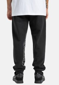 Schwarze Jogginghose mit lockerer Passform, mit weißen grafischen Texten entlang des linken Beins. Rippbündchen und elastischer Bund; aus weichem Material hergestellt.