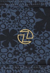 Tissu bleu avec un motif floral et circulaire en noir, accompagné d'un logo circulaire doré et d'une couture matelassée contrastante.