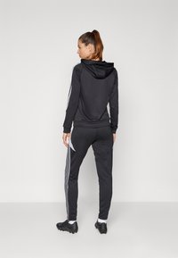 Black athletic tracksuit with a hood, featuring white stripes on sleeves and sides. Soft fabric with fitted design and tapered pants.