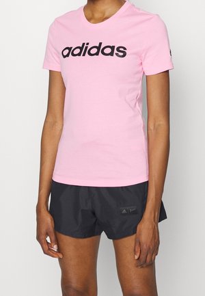 Personne portant un t-shirt rose Adidas avec un logo noir et un short noir Adidas avec un petit logo sur la cuisse gauche.
