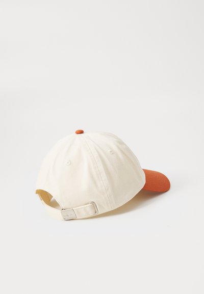Cotton cap in cream with an orange visor and top button. Features an adjustable metal strap at the back. Simple, structured design.