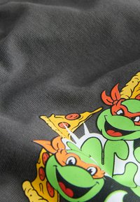 Ciemnoszara tkanina z kolorową grafiką przedstawiającą kreskówkowe żółwie i pizzę. Wzór zawiera zielone żółwie z pomarańczowymi i czerwonymi akcentami.