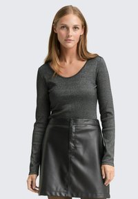 Długi rękaw bluzki z teksturowanej czarnej tkaniny z metalicznymi błyskami, zestawiony z czarną skórzaną spódnicą o wysokim stanie z przednim zapięciem na guzik.