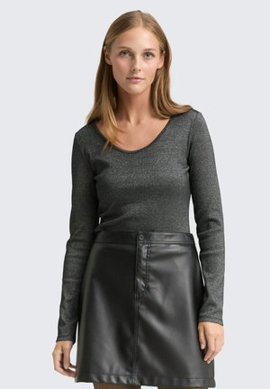 Haut à manches longues en tissu texturé noir avec des étincelles métalliques, associé à une jupe en cuir noir taille haute avec un bouton sur le devant.