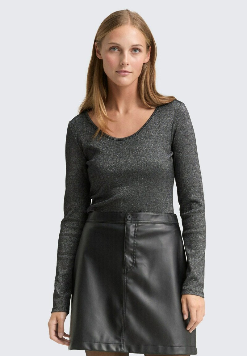 Długi rękaw bluzki z teksturowanej czarnej tkaniny z metalicznymi błyskami, zestawiony z czarną skórzaną spódnicą o wysokim stanie z przednim zapięciem na guzik.
