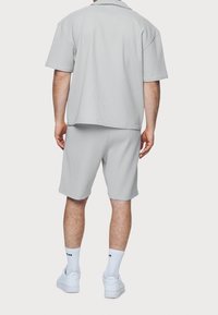 Chemise grise à manches courtes côtelée et short assorti, en tissu texturé. Des baskets blanches et des chaussettes complètent la tenue.