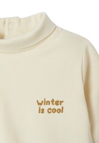 Hellbeiger Pullover mit hohem Kragen. Besitzt eine weiche Textur und eine gestickte Phrase "Winter ist cool" in brauner Schrift.