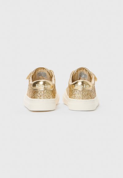 Um par de sapatilhas de glitter dourado para crianças com solas brancas, visto de trás, exibindo a marca Polo nas abas do calcanhar.