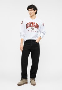 Λευκό πουκάμισο με μακριά μανίκια και κόκκινο τύπωμα "ICECREAM DESIGN", μαύρο τζιν και μπεζ μποτάκια, με υφασμάτινες υφές και casual εφαρμογή.