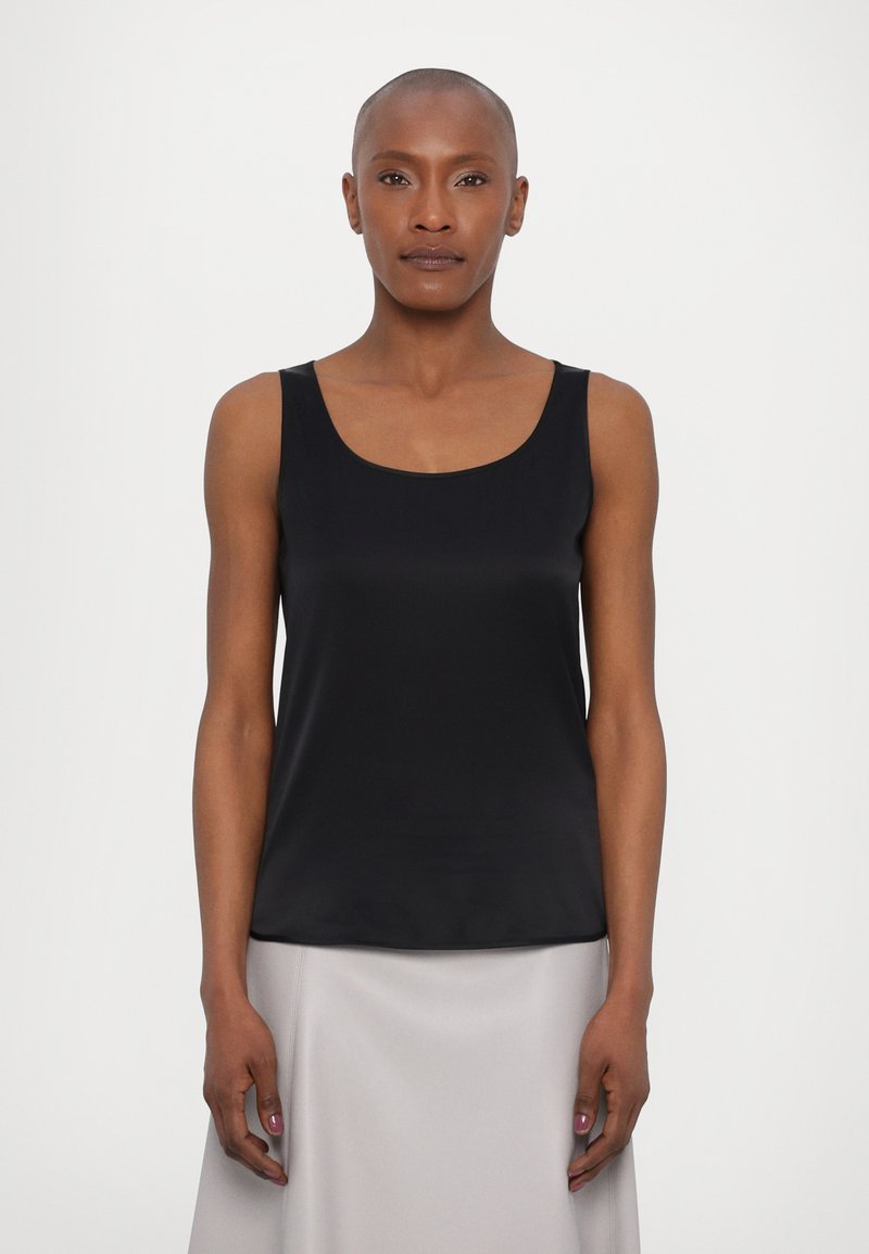 Black sleeveless top in smooth fabric, featuring a rounded neckline and a relaxed fit. Paired with a light gray skirt.