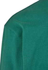 Camiseta de manga corta en tejido de algodón verde profundo, con una textura suave y escote redondo, detalles en las costuras de los hombros y sin patrones.