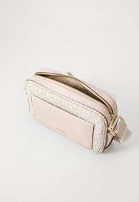 Světle růžová crossbody taška s monogramovým vzorem, dvěmi zipovými přihrádkami a přední kapsou. Zlaté kovové akcenty a nastavitelné rameno.