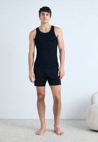 Schwarzes Baumwoll-Tanktop und Shorts-Set. Enganliegendes Design, glatte Textur, minimale Markenkennzeichnung auf der Brust, und die Shorts verfügen über einen elastischen Taillenbund.