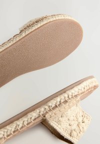 Beige espadrille slip-on met een geweven jute bovenzijde, ronde neus en een gestructureerde rubberen zool met een gladde afwerking.