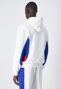 Sweatshirt à capuche blanc, avec des accents bleu et rouge sur les manches. Texture douce, coupe décontractée, poignets et ourlet côtelés.