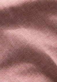 Gros plan sur un tissu marron clair à la texture avec un motif de maille en zigzag fin et des plis doux.