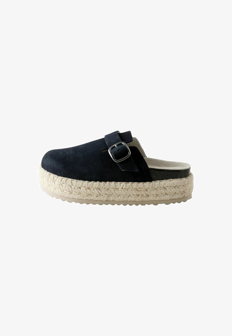 Chaussure slip-on en daim noir avec une boucle argentée, une semelle plateforme épaisse en jute tissé, et une semelle intérieure beige, vue de profil.