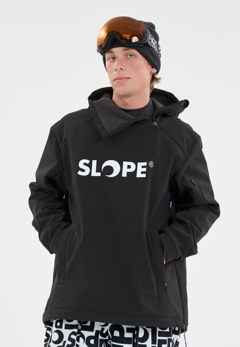 Sort skijakke med grå accenter og høj krave, der har et fremtrædende hvidt "SLOPE" logo. Modellen bærer orange skibriller og mønstrede bukser.