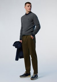 Suéter de punto gris, pantalones verde oliva, zapatillas azul con acentos, y una chaqueta azul marino colgada del brazo. Diseño simple y de corte recto.