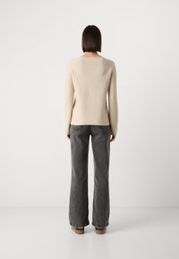 Suéter beje de mangas compridas com decote retangular, combinado com jeans cinzentos de perna larga. O conjunto apresenta uma textura suave e um design simples.