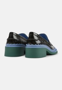 Chaussures en cuir verni noir à bout arrondi, avec un talon épais vert, une semelle bleue et un détail de bord en zigzag.