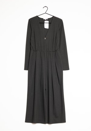 Tuta nera con maniche lunghe, scollatura a V, vita elasticizzata e gambe ampie; presenta un piccolo accessorio dorato e un'etichetta del prezzo attaccata.