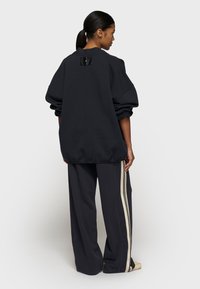 Übergroßer schwarzer Pullover mit einem strukturierten Rückenteil, kombiniert mit lockeren schwarzen Hosen und cremefarbenen Seitenstreifen.