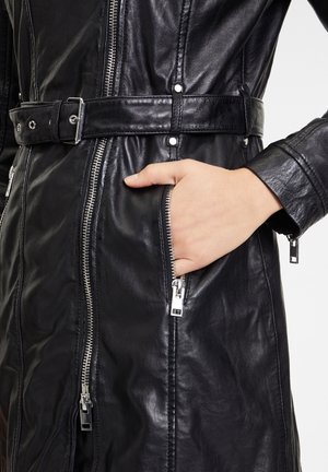 Hand in pocket of black leather jacket with silver zippers and belt, showing detailed stitching and texture of the material.