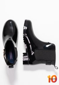 Botas de lluvia negras y brillantes con punta redondeada, paneles laterales elásticos y suela texturizada. Incluye una pestaña para facilitar su puesta.