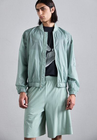 Veste bomber vert clair avec des poignets élastiques, assortie à un short vert clair. Le tissu est lisse avec un léger éclat.