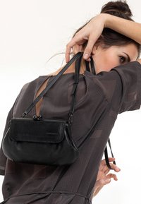 Schwarze Lederhandtasche mit Klappenverschluss und dekorativem Verschluss. Sie verfügt über verstellbare Träger und eine glatte Textur.