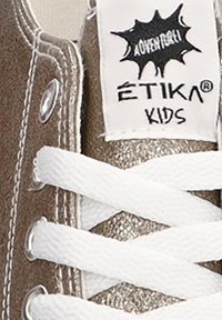 Zapatilla de cuero marrón con cordones blancos, una textura metálica brillante y una etiqueta negra de "ÉTIKA KIDS" con acentos gráficos.