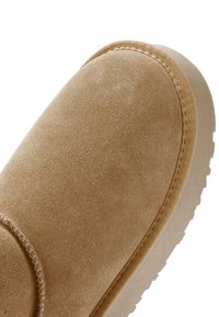 Gros plan sur l'avant d'une chaussure en daim beige avec des coutures visibles et le bord de la semelle en caoutchouc texturé.