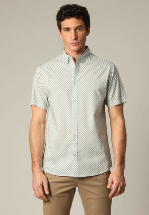 Chemise à manches courtes bleu clair avec bouton, présentant un motif géométrique avec des accents bleu foncé. Le tissu a une texture lisse et le style est ajusté.