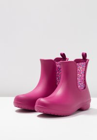 Stivaletti rosa in gomma con lati testurizzati decorati da un motivo a puntini colorati. Sono dotati di linguette per facilitare la calzata e hanno una finitura liscia.