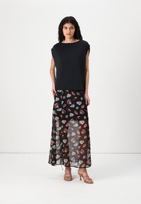 Top negru cu mânecă scurtă și croi lejer, asociat cu o fustă neagră transparentă, decorată cu modele colorate de scoici. Modelul poartă sandale cu barete.