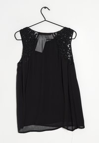 Zwarte mouwloze blouse van doorschijnende stof, met textuur in bloemenkant op de schouders en een gebogen zoom. Hangt aan een zwarte haak.