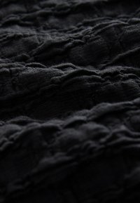 Tissu noir texturé présentant un motif froissé, mettant en valeur un matériau doux avec des crêtes et des profondeurs variables pour un intérêt visuel.