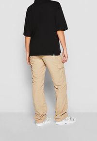 Černé oversized tričko s krátkým rukávem, spárované s béžovými cargo kalhotami se bočními kapsami a bílými sportovními botami.