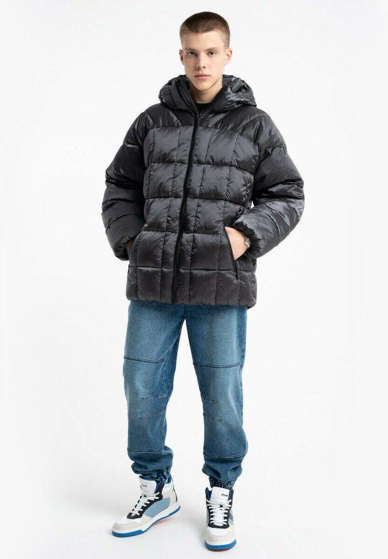 Czarna kurtka puchowa z kapturem, pikowany wzór, zamek z przodu i kieszenie po bokach. W połączeniu z jasnoniebieskimi dżinsami i wysokimi trampkami.