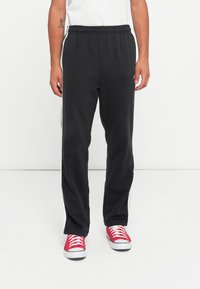 Black sweatpants made of soft fabric, featuring a relaxed fit, elastic waistband, and white side stripes, paired with red sneakers.