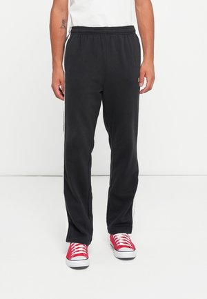 Black sweatpants made of soft fabric, featuring a relaxed fit, elastic waistband, and white side stripes, paired with red sneakers.
